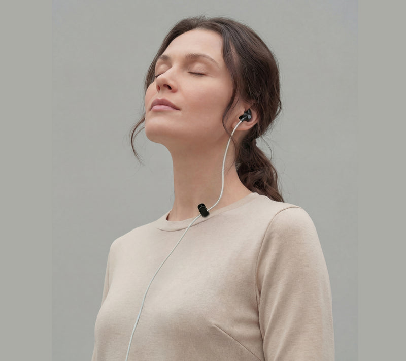 Woman using ZenoWell earpiece for vagus nerve stimulation, promoting relaxation and stress relief through transcutaneous auricular vagus nerve stimulation (taVNS).